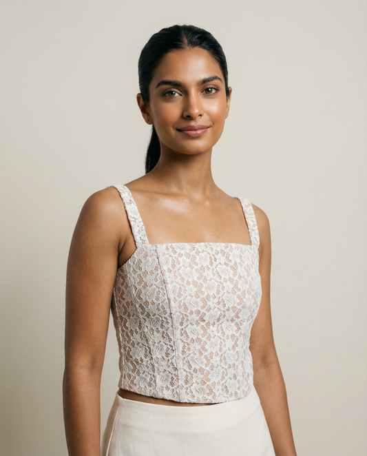Woman wearing a beige lace top and white pants against a neutral background